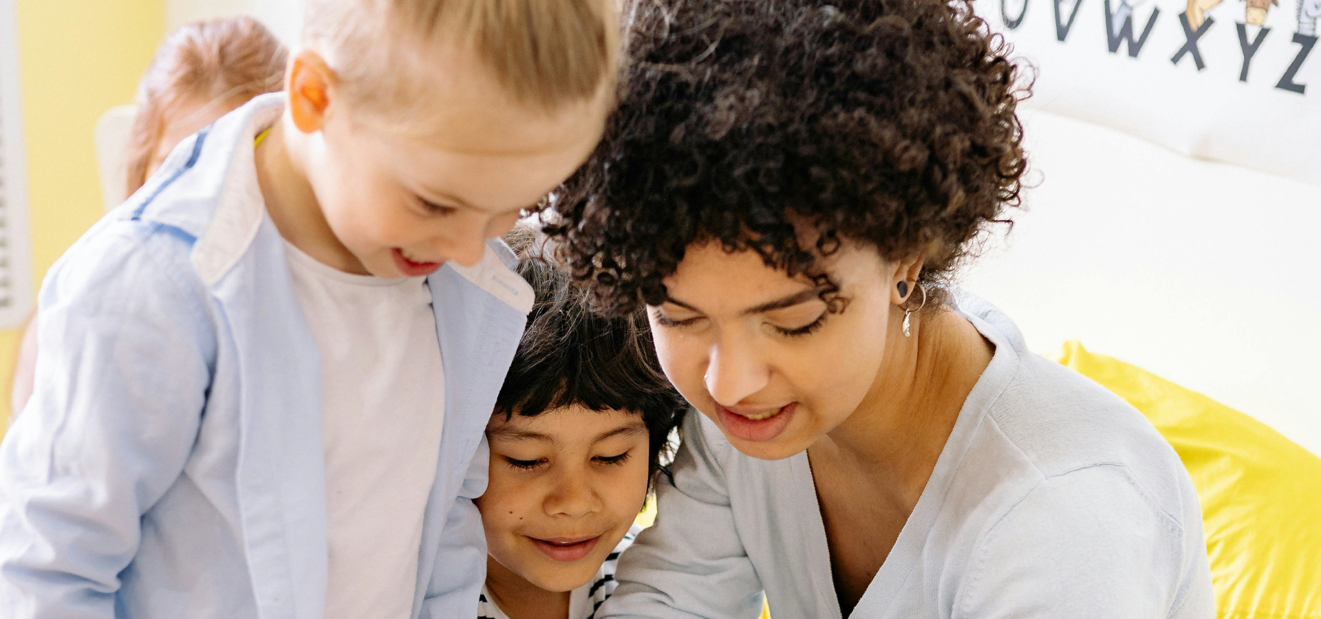 Kinder schauen gemeinsam mit einer Fachkraft lächelnd auf ein Tablet