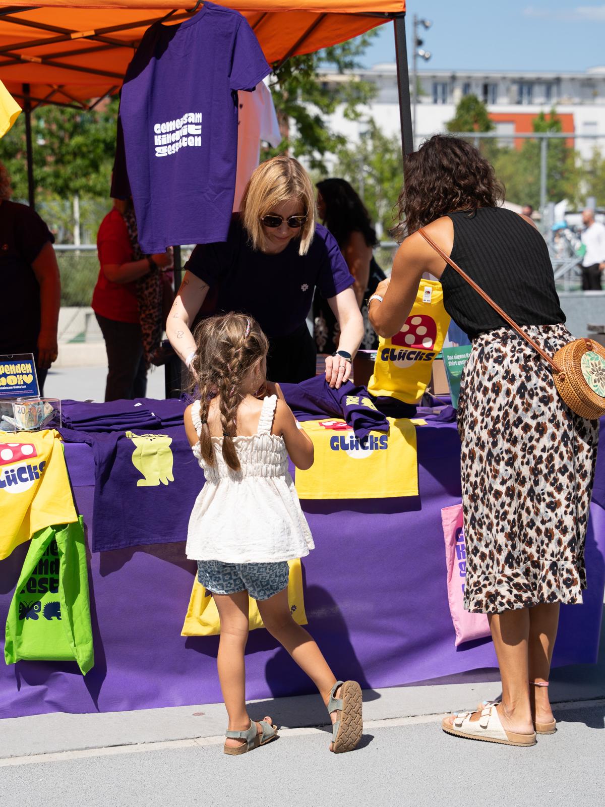 Besucherinnen und Kind am Merchandise-Stand des Sommerfests.