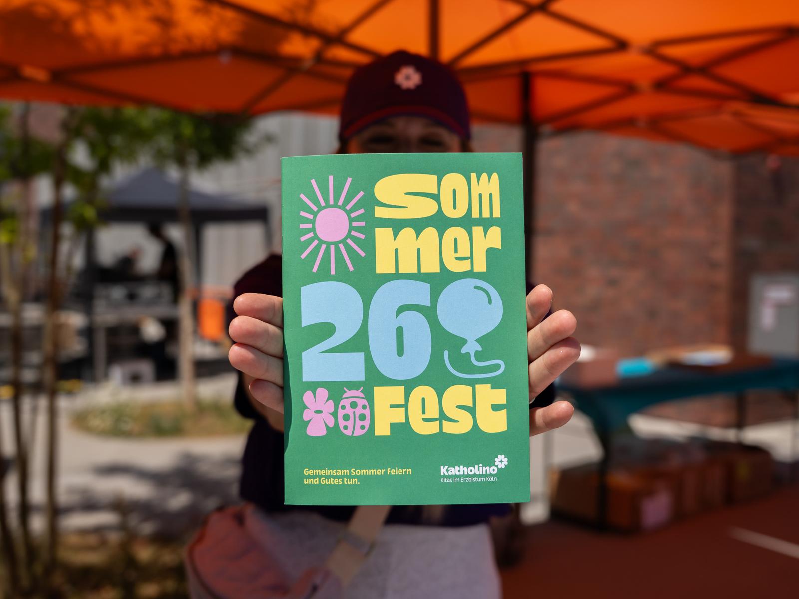 Person hält eine Broschüre für das Sommerfest 2026.